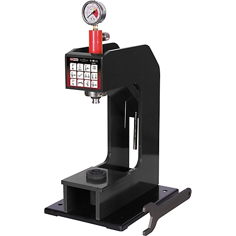 Schwarze Hydraulikpresse mit Manometer und rotem Ventil. Auf einer schwarzen Grundplatte liegt ein Schraubenschlüssel.